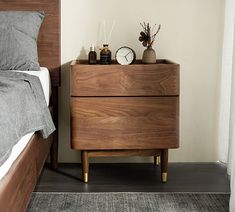 a nightstand with two clocks on it next to a bed