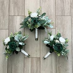 three bridal bouquets on the floor with greenery and white roses in them