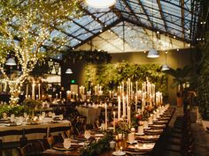 an indoor dining room with tables and chairs covered in greenery, lit by candles