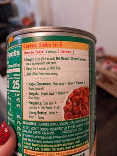 a can of canned food sitting on top of a wooden table next to a person's hand