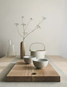 a wooden table topped with bowls and a vase filled with flowers on top of it