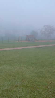 a park bench sitting in the middle of a foggy field with a playground in the background