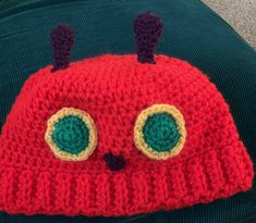 a crocheted red hat with green eyes and ears