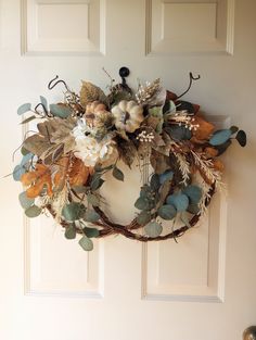 a wreath hanging on the front door with leaves and flowers in it, next to a white door