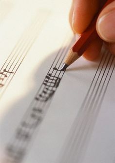 a person holding a pencil and writing on sheet music