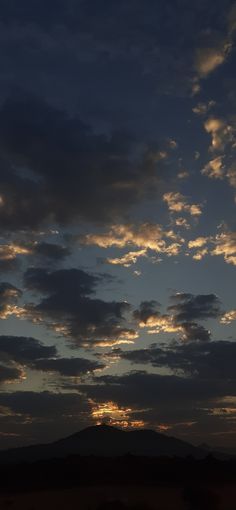 the sun is setting behind some clouds in the sky over a hill and plain area