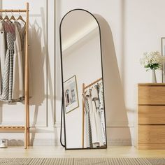 a mirror sitting on top of a wooden floor next to a dresser and clothes rack