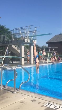 a person jumping into a swimming pool with their arms in the air while others watch