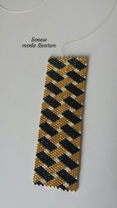 a piece of beaded fabric with black and gold designs on the front, sitting on a white surface