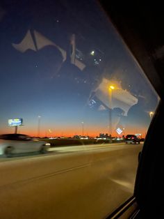 the view from inside a vehicle driving down a highway at night with lights and buildings in the background