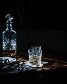 an empty glass sitting on top of a wooden table next to a decanter