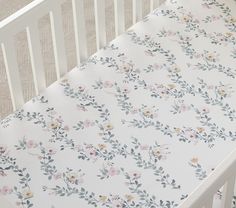 a white crib bed with a floral print on it and the words pottery barn kids