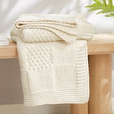 a white knitted blanket sitting on top of a wooden bench next to a plant