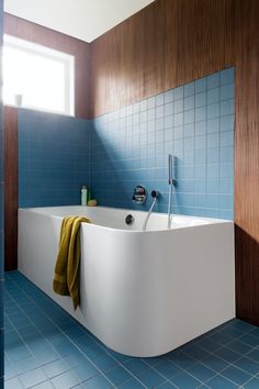 a bathtub in a bathroom with blue tiles on the walls and floor, next to a window