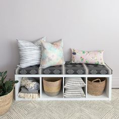 a white bench with several pillows and baskets on the bottom, along with other decorative items