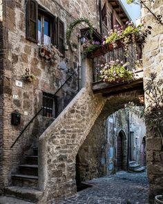 an old stone building with flowers growing on the balconies and stairs leading up to it