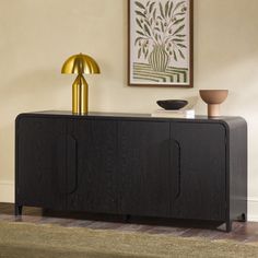 a black sideboard with two gold lamps on top and a painting hanging above it