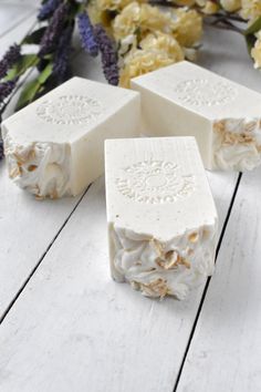 three pieces of soap sitting on top of a white wooden table next to flowers and dried herbs