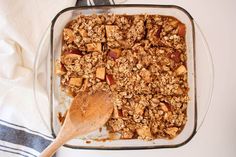 a glass baking dish filled with granola and apple slices next to a wooden spoon