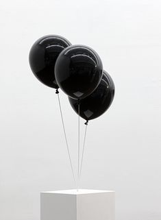 three black balloons floating in the air on top of a white pedestal with string attached