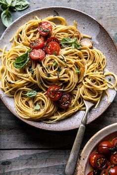 a plate of pasta with tomatoes and basil on the side next to a bowl of cherry tomatoes