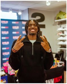 a young man with dreadlocks standing in front of a store display and giving the peace sign