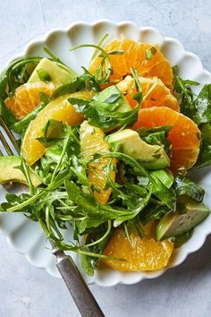 a salad with oranges and avocado in a white bowl on a table