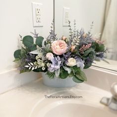 a vase filled with flowers sitting on top of a bathroom sink next to a mirror