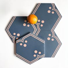 an orange sitting on top of two coasters that are shaped like hexagons