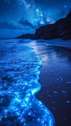 an ocean beach with blue lights on the water and stars in the sky above it