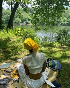 a woman sitting on top of a blanket next to a tree covered field and river