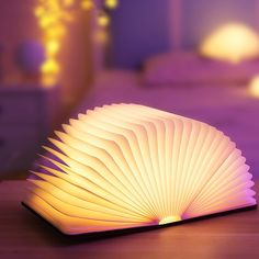 an open book sitting on top of a wooden table next to a night light in the shape of a fan