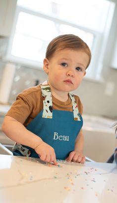 a little boy sitting at a table with sprinkles on his bib