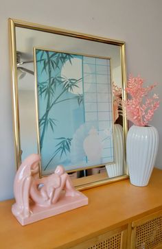 a pink elephant figurine sitting on top of a wooden dresser next to a mirror