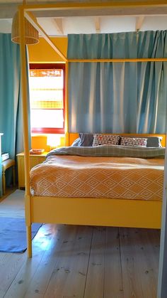 a yellow bed frame in a bedroom with blue curtains on the windowsill and wood flooring