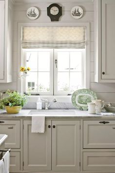 a kitchen with white cabinets and green plates on the window sill above the sink