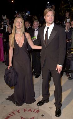 a woman in a black dress and a man in a tuxedo holding hands