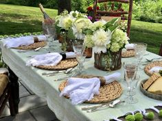 an outdoor table set with place settings for two people and flowers in vases on the table