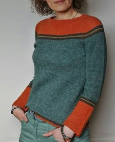 a woman in an orange and green sweater is leaning against a wall with her hands on her hips