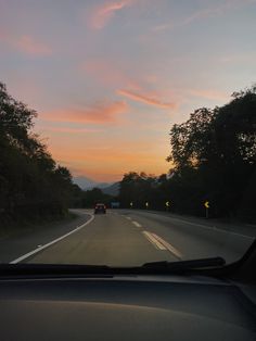 the sun is setting on an empty road with trees and mountains in the back ground