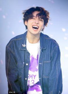 a young man wearing a denim jacket and smiling at the camera with his mouth open