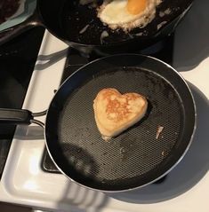 two pans with food cooking on top of them and one has an egg in the shape of a heart