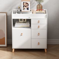 a white cabinet with drawers and pictures on the top shelf next to a framed photograph