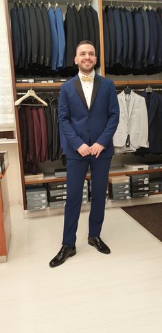 a man in a tuxedo standing in front of a closet full of men's clothing