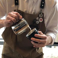 a man in an apron is pouring something into a cup while holding a coffee mug