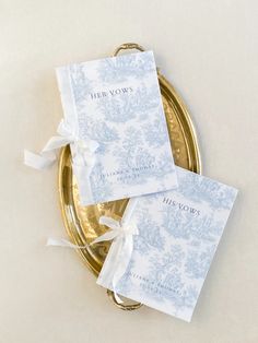 two blue and white napkins sitting on top of a gold plate next to each other