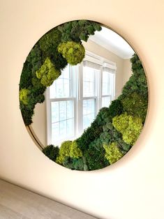 a circular mirror covered in green plants next to a window