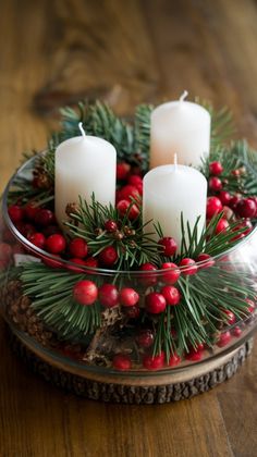 three candles are sitting in a glass bowl with holly and red berries on the table