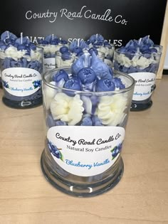 blue and white flowers are in a clear glass cup on a table with a sign behind it