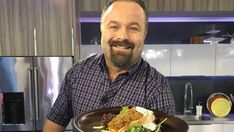 a man standing in front of a kitchen holding a plate with meat and vegetables on it